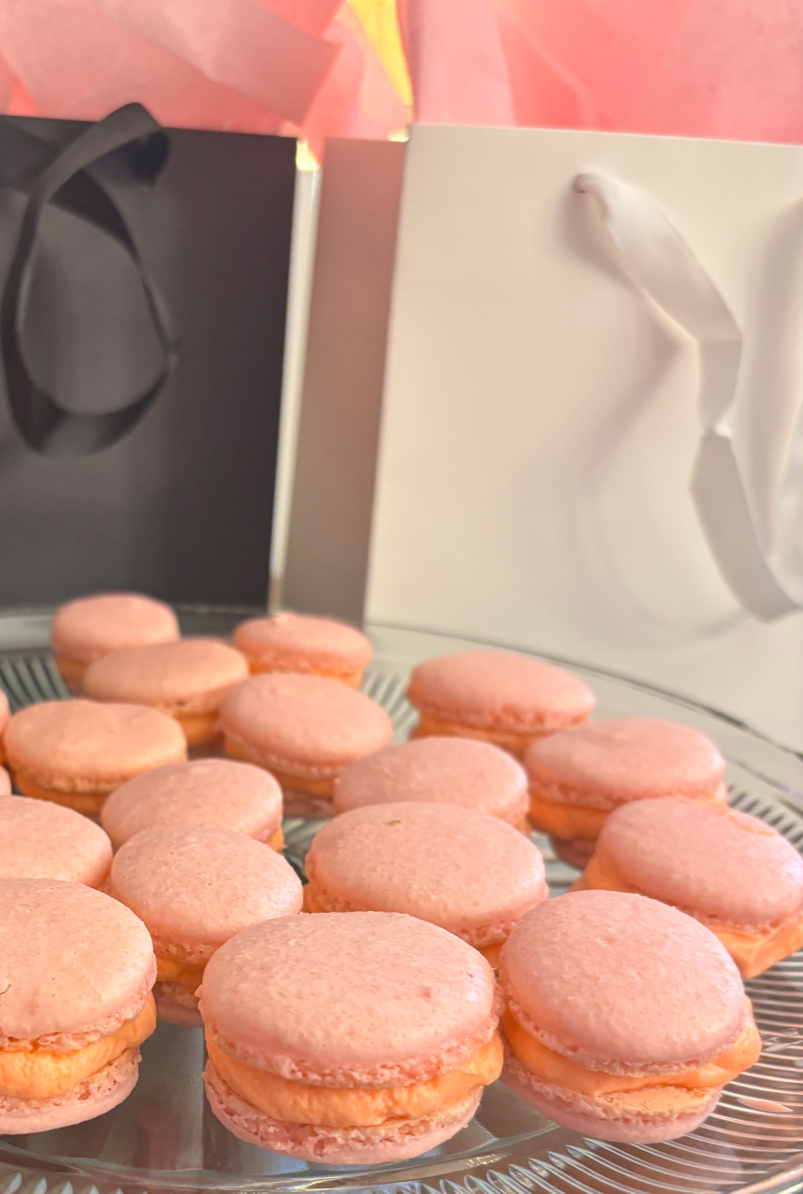 pink macarons on a glass serving dish with black and white gift bags in the background