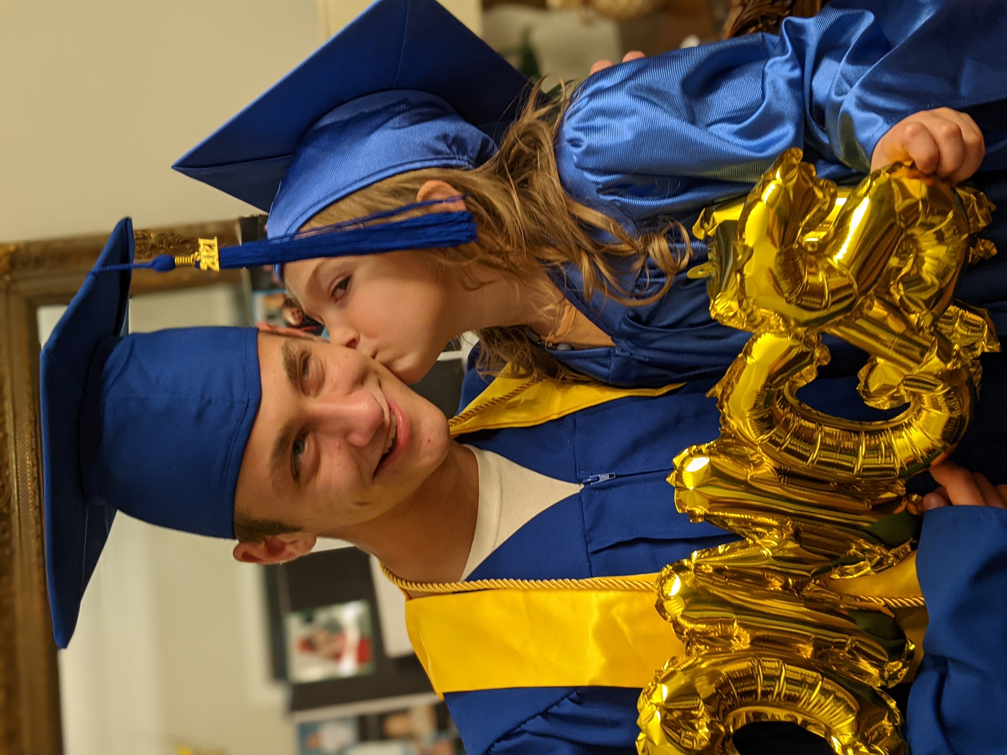 kindergarten graduate kissing highschool graduate's cheek